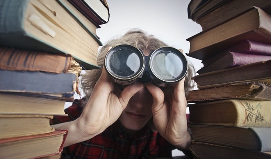 Foto: Andrea Piacquadio Anonyme Person Mit Fernglas, Die Durch Gestapelte Bücher Schaut