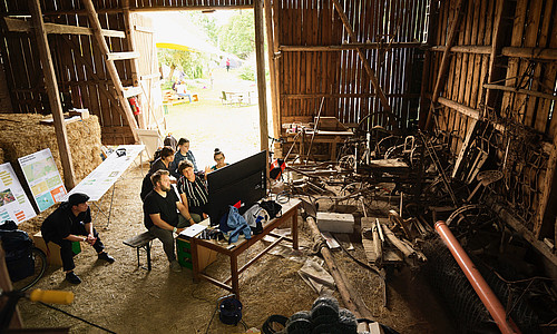 Mehrere Personen sitzen vor Bildschirm in einer Scheune