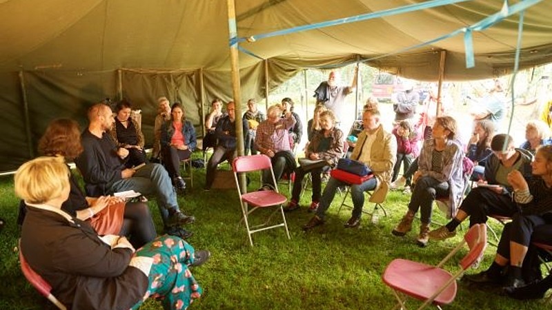 Menschen sitzen im Diskussionskreis unter einem Zelt