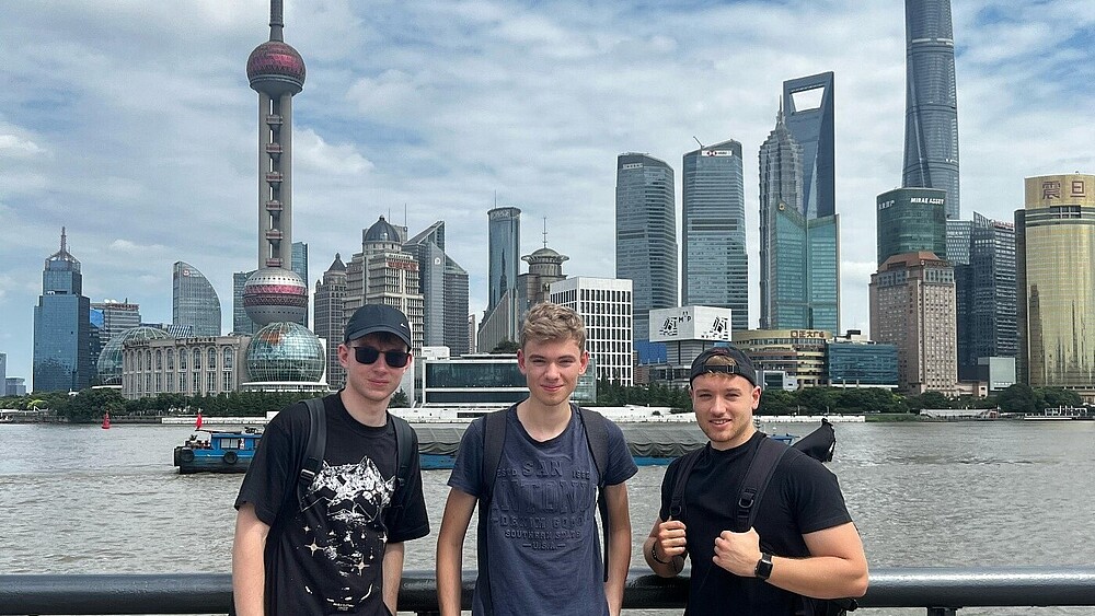 Drei Studenten stehen auf einer Aussichtsplattform vor der Skyline von Shanghai.