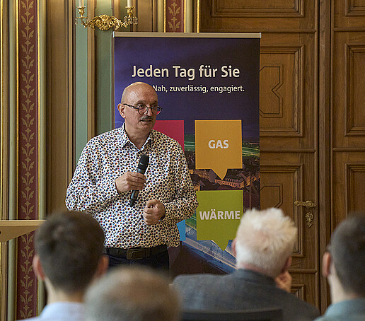 Ein Teilnehmer steht vor einem Roll-up und spricht in ein Mikrofon.