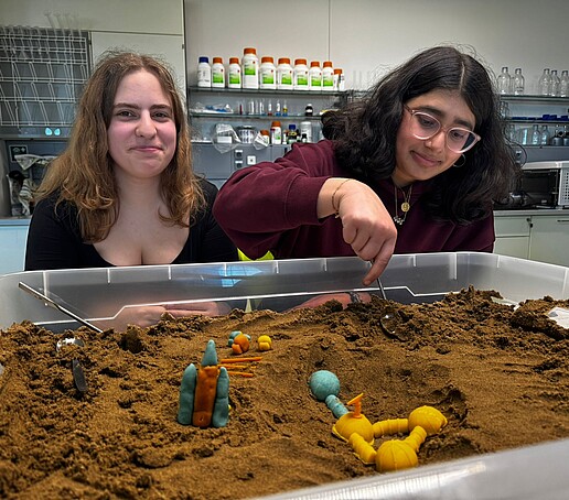 Zwei Mädchen sitzen vor einer Sandbox.