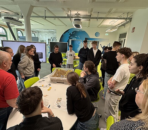 Schülerinnen und Schüler stehen um einen Tisch herum.