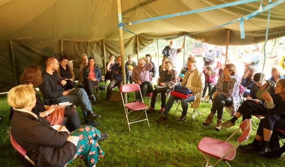 Menschen sitzen im Diskussionskreis unter einem Zelt