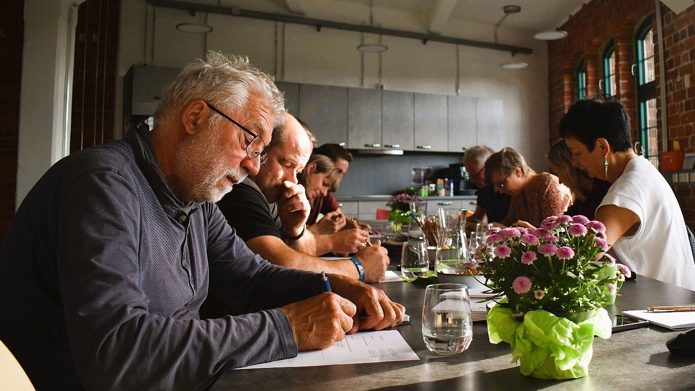 Workshopteilnehmende sitzen an einem Tisch im Celsiuz und machen sich schriftliche Notizen.
