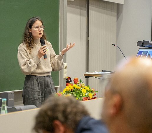 Eine Frau spricht in ein Mikrofon vor dem Publikum.
