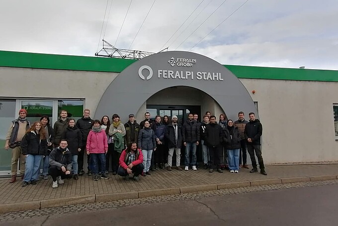 Eine Gruppe Studierender steht vor dem Haupteingang der Feralpi Stahl.