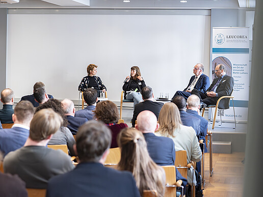 Podium mit 4 Personen vor Zuschauern