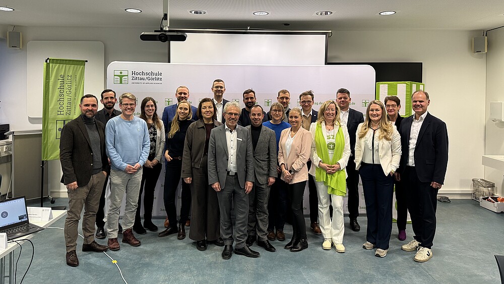 Mehrere Menschen stehen als Gruppe vor einer weißen Pressewand und lächeln in die Kamera.