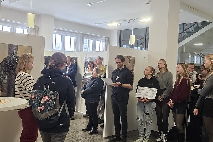 Silvio Thamm verliest die Gewinner vor stehendem Publikum. Neben ihm steht eine Frau, die einen Preisgeldscheck in den Händen hält.