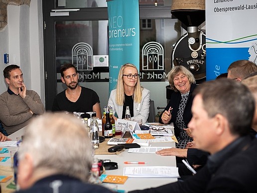 Teilnehmende an den Vorbereitungen des Erzählsalons sitzen am Tisch und untrhalten sich.