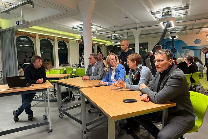 Professorin Keil und Beratungspersonen sitzen im School Lab an Tischen und unterhalten sich.