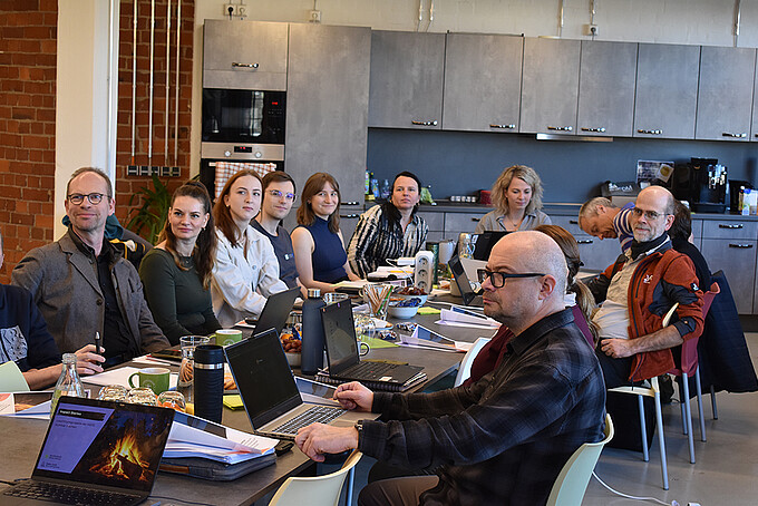 Am vollbesetzten Tisch sitzen die Workshopteilnehmenden und lauschen dem Vortrag.